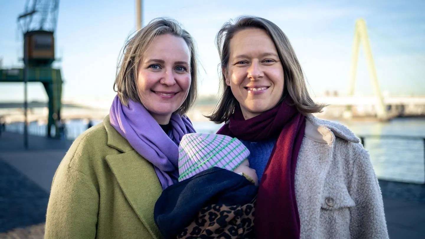 Zwei Frauen halten ein Baby im Arm, eine dritte Frau lächelt sie an.