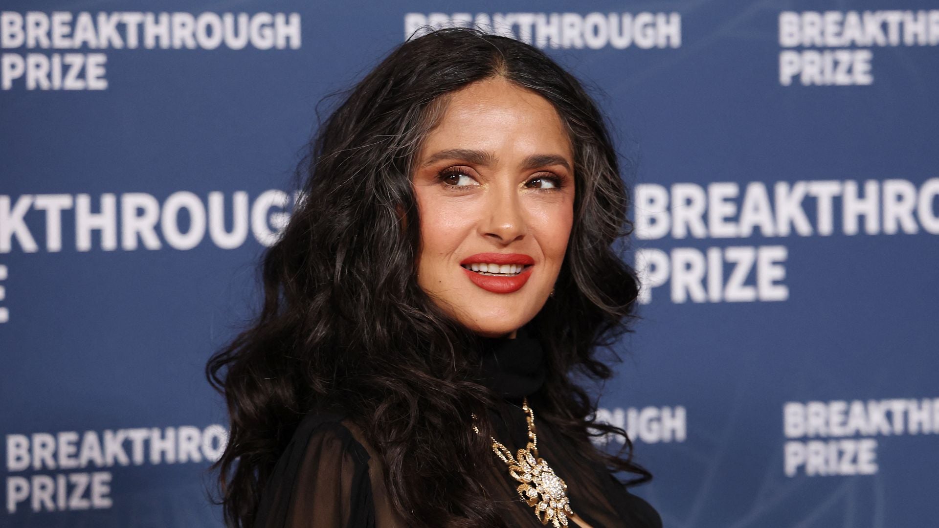 Salma Hayek sitzt auf der Tribüne bei den French Open und lächelt.